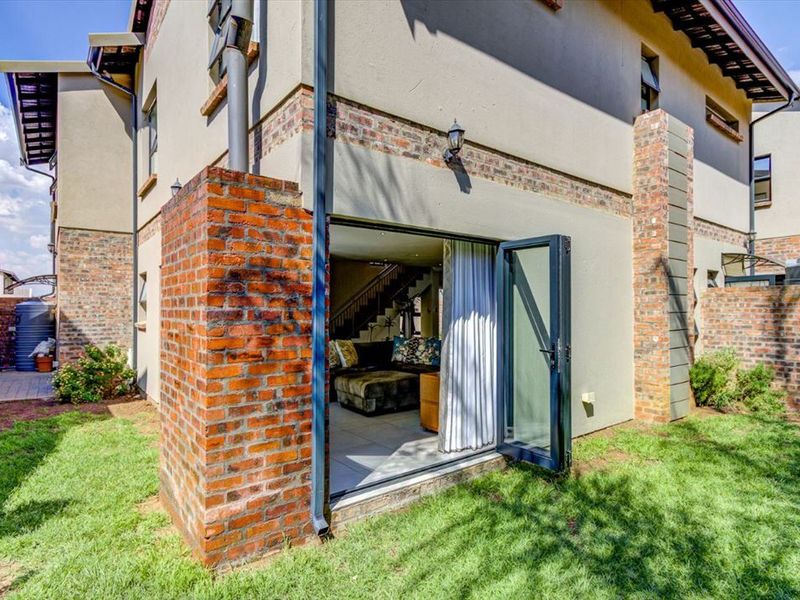 Rear view of the property featuring exposed brick accents, a small lawn, and bi-fold doors providing seamless access to the interior living space.