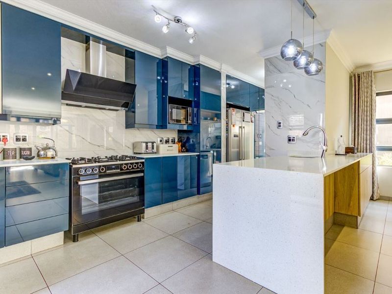 Modern kitchen featuring high-gloss blue cabinetry, a stone-topped island, integrated appliances, and elegant marble-look splashbacks with contemporary pendant lighting.
