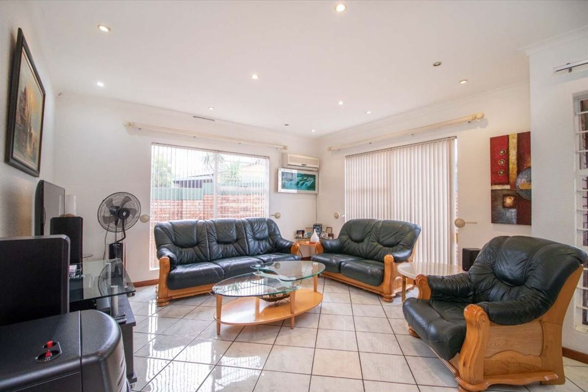 A bright living room featuring tiled flooring, recessed downlights, and a wall-mounted split-system air conditioner, with large windows providing natural light.