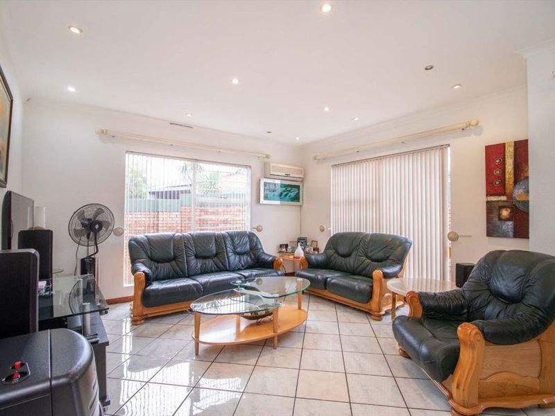 A bright living room featuring tiled flooring, recessed downlights, and a wall-mounted split-system air conditioner, with large windows providing natural light.