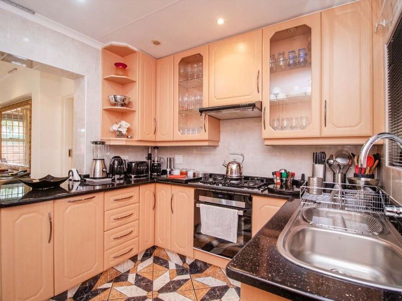 A functional kitchen featuring light wood cabinetry, dark granite countertops, a gas hob, built-in oven, and decorative tiled flooring.