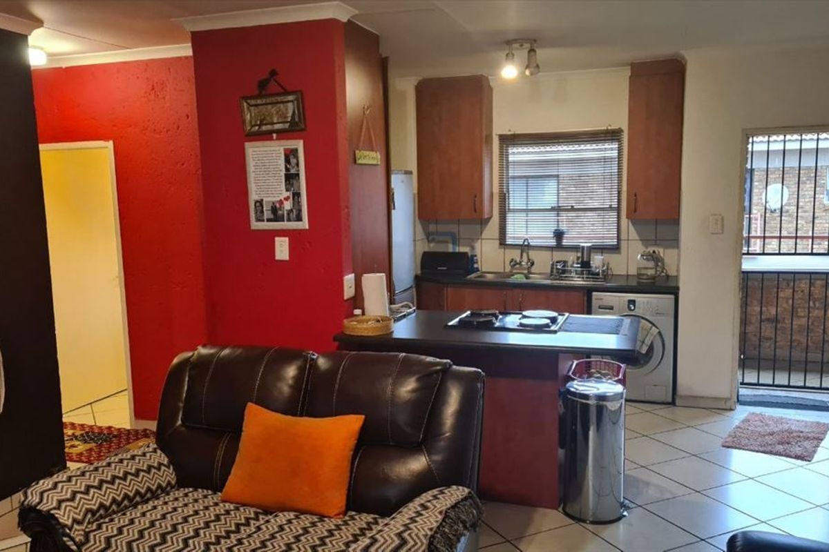 Open-plan living area featuring a compact kitchen with built-in cabinetry, gas hob, and direct access to an exterior balcony area.