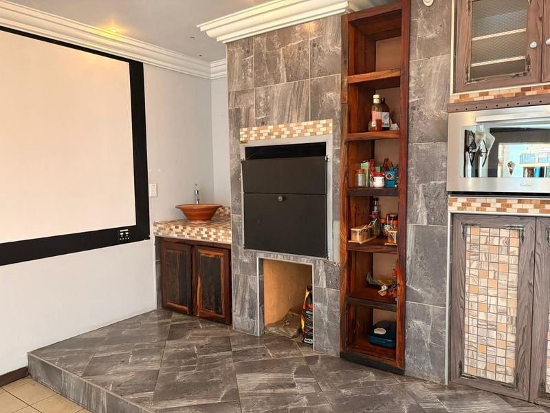 Covered entertainment area featuring a built-in braai, tiled finishes, integrated oven, and custom cabinetry with a basin, ideal for hosting and outdoor dining.