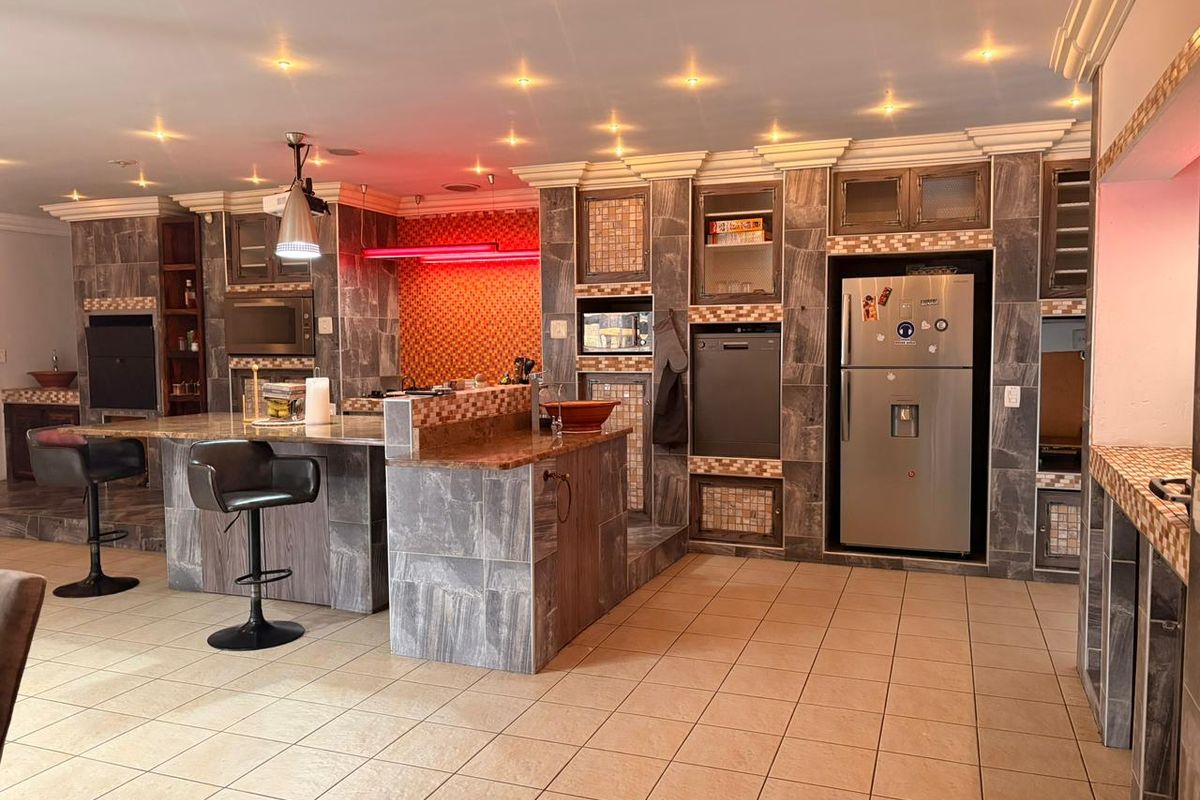 Spacious kitchen featuring extensive stone tile finishes, granite countertops, a central island, and integrated appliances with modern recessed lighting.