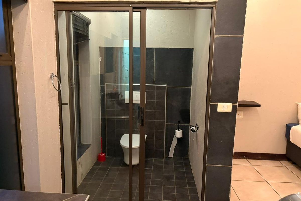 A compact bathroom featuring a sliding glass door, dark tiled walls and flooring, and a wall-mounted toilet.