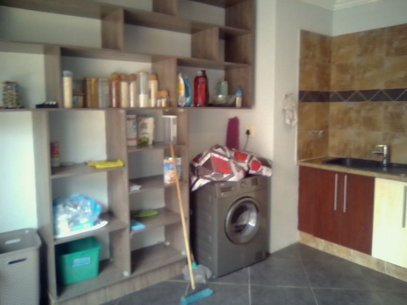 A functional laundry area featuring built-in shelving, cabinetry, a sink, and tiled splashback.