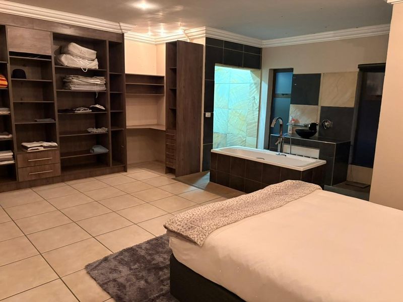 Spacious bedroom featuring integrated cabinetry, tiled flooring, and an open-plan en-suite bathroom with a built-in bathtub and vanity.