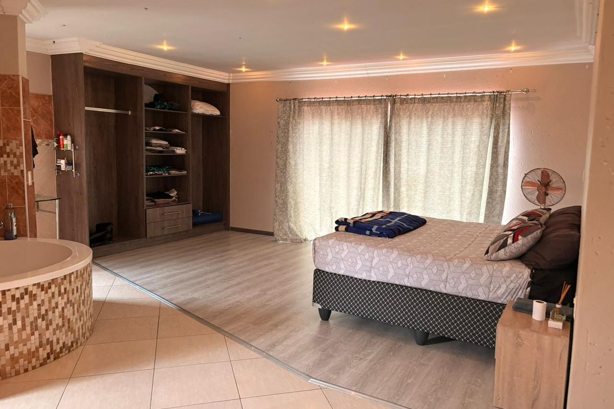 Spacious bedroom featuring integrated storage, recessed lighting, and an open-plan en-suite bathtub area with a mix of tiled and laminate flooring.