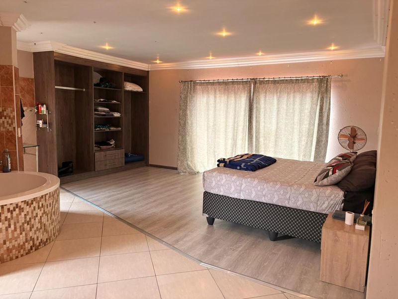 Spacious bedroom featuring integrated storage, recessed lighting, and an open-plan en-suite bathtub area with a mix of tiled and laminate flooring.
