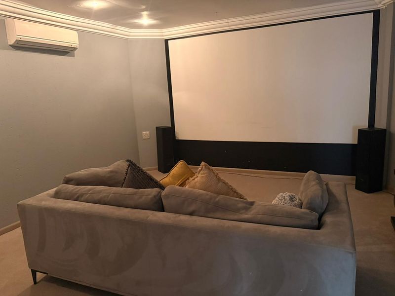 Dedicated cinema room featuring a large projector screen, wall-mounted air conditioning unit, and carpeted flooring.