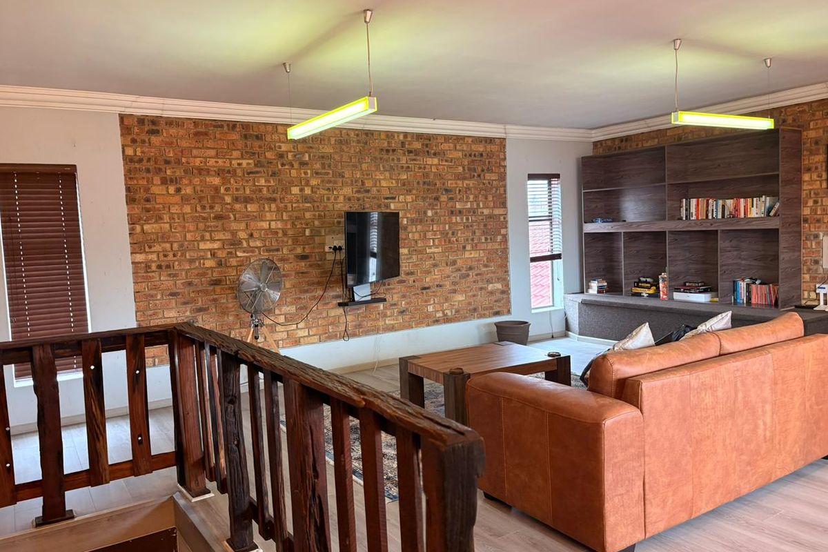 Spacious living area featuring an exposed brick feature wall, built-in timber shelving, and a rustic staircase railing, creating a warm and inviting atmosphere.