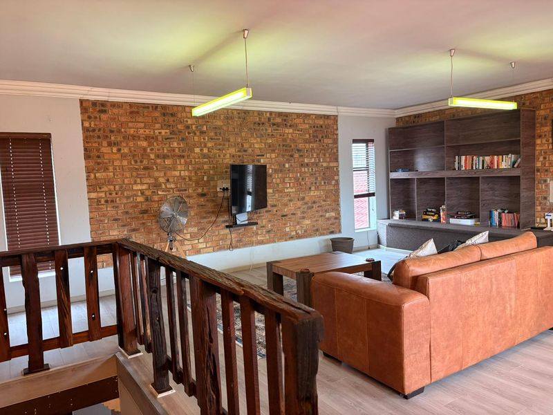 Spacious living area featuring an exposed brick feature wall, built-in timber shelving, and a rustic staircase railing, creating a warm and inviting atmosphere.