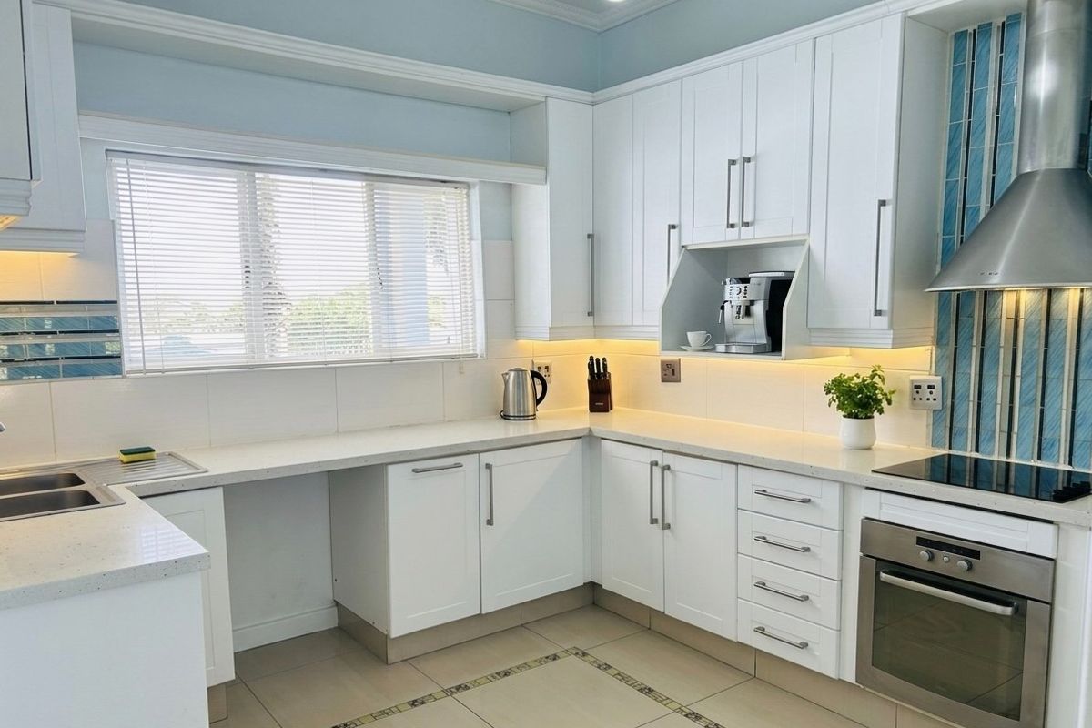 A well-maintained kitchen featuring white shaker cabinetry, stone countertops, integrated stainless steel appliances, and modern under-cabinet lighting.