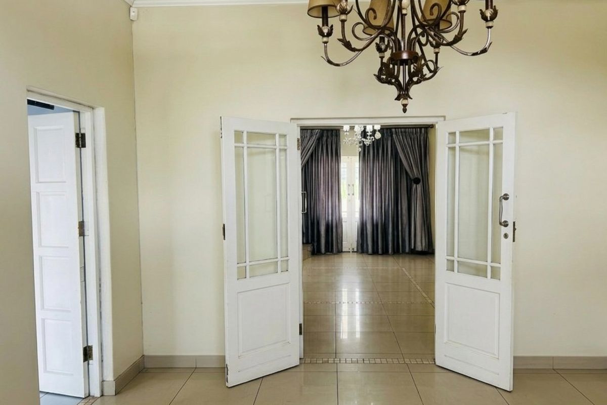 A bright and spacious living area featuring neutral tiled flooring, elegant cornicing, and double glass-panelled doors leading to an adjoining room.