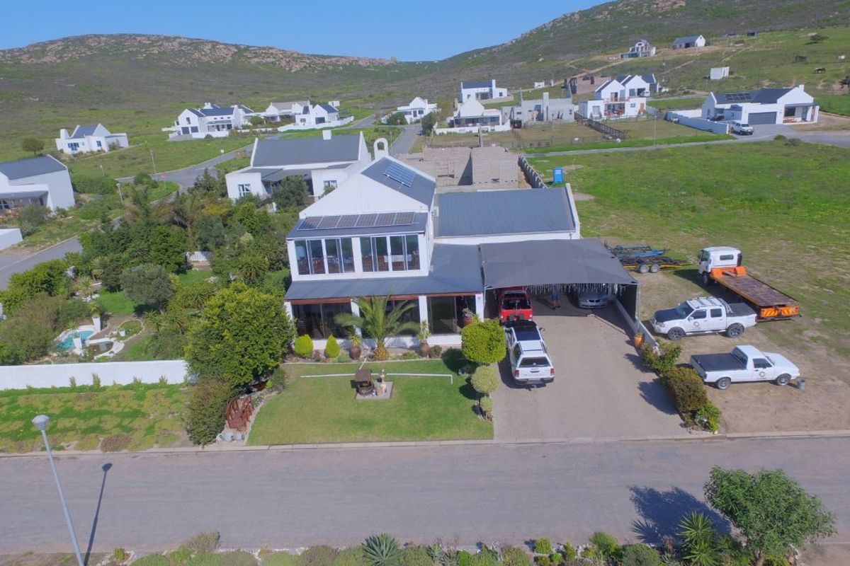 Aerial view of a residential property featuring a metal roof, solar panels, a paved driveway with a carport, and surrounding landscaped grounds.