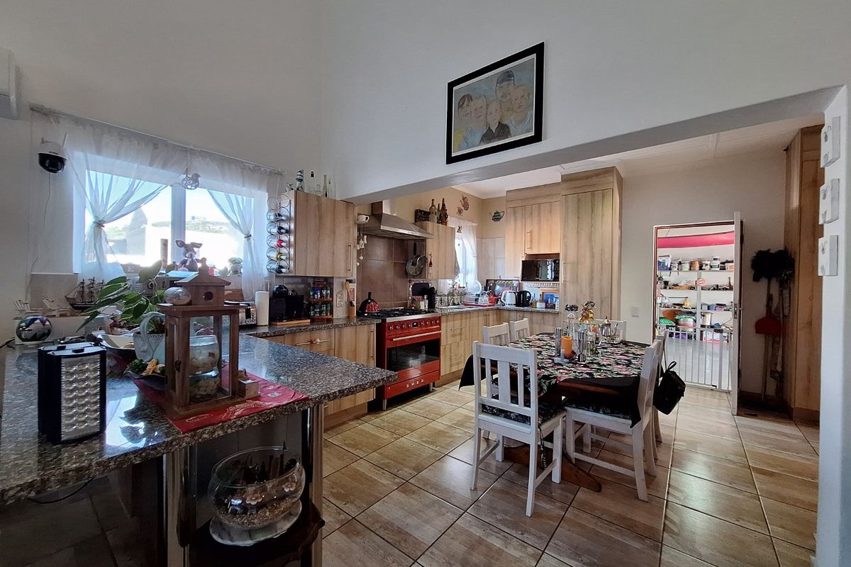 Spacious kitchen featuring granite countertops, wood-finish cabinetry, a distinctive red oven, and tiled flooring, with an open-plan layout leading to a scullery area.