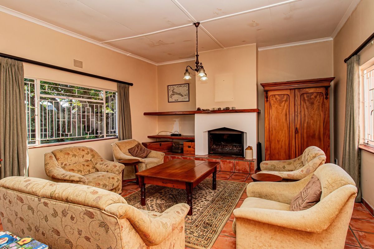 A traditional living room featuring a built-in fireplace, terracotta tiled flooring, and large windows with security bars, requiring some ceiling maintenance.