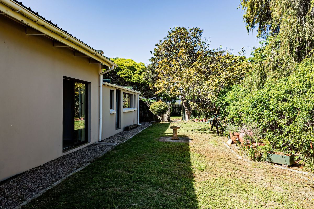 A view of the rear exterior of the house featuring a lawn, gravel pathway, and sliding glass door access to the interior.