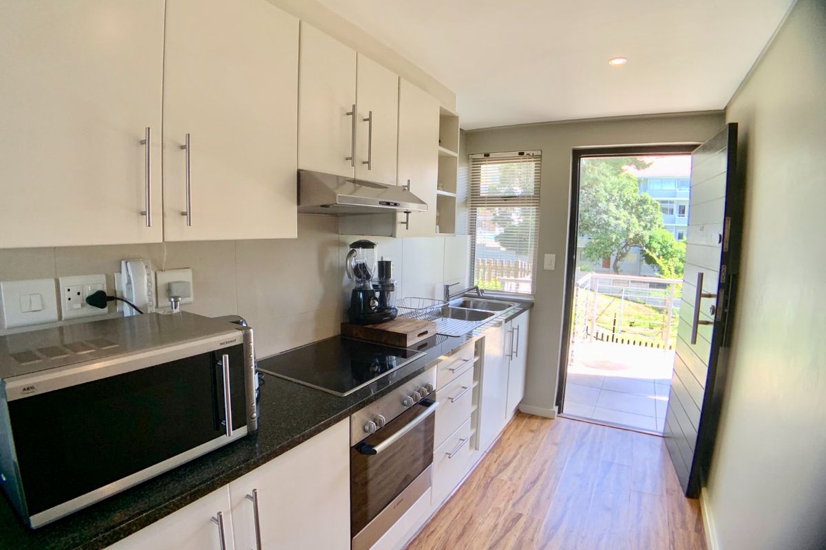 Modern galley-style kitchen featuring white cabinetry, granite countertops, integrated oven and hob, and direct access to an outdoor balcony area.