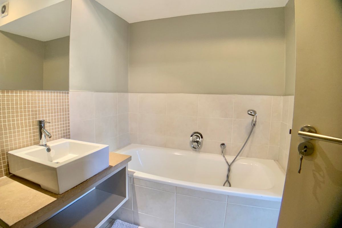 A clean, modern bathroom featuring a vessel sink, built-in bathtub with handheld shower attachment, and neutral wall tiling.