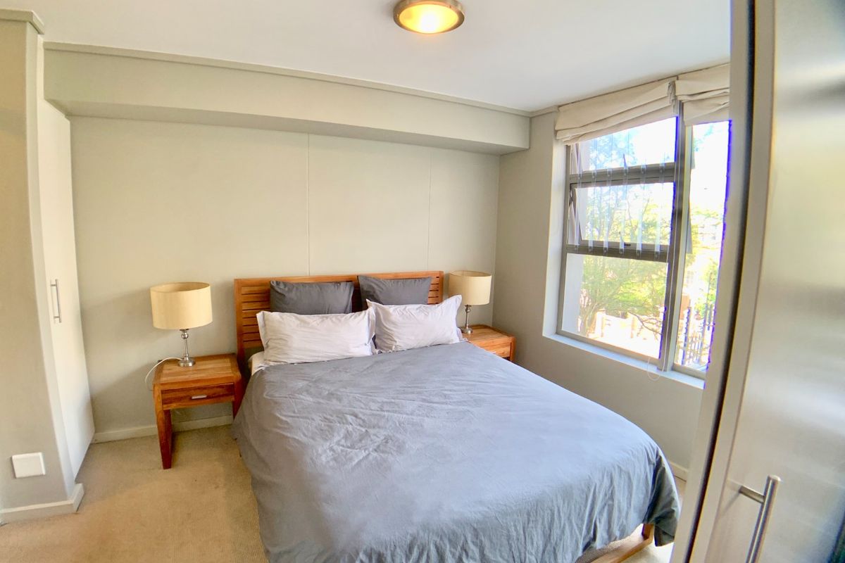 A well-maintained bedroom featuring neutral wall tones, carpeted flooring, a built-in wardrobe, and a window providing natural light.