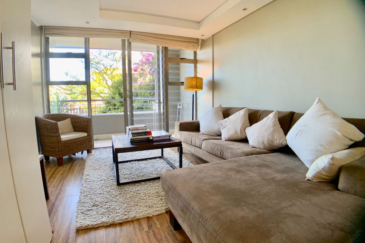A bright living room featuring laminate flooring, recessed ceiling lights, and large sliding glass doors that open onto a private balcony.