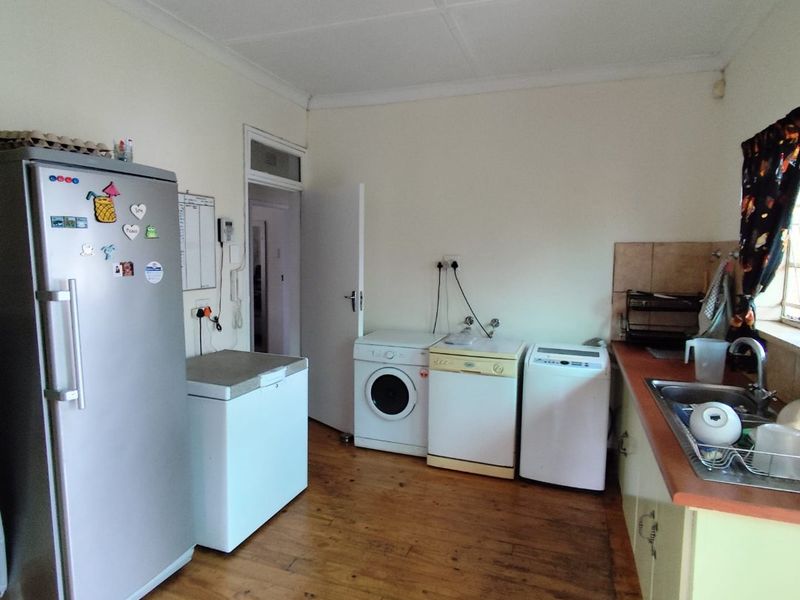 A functional laundry room featuring timber flooring, built-in cabinetry, a stainless steel sink, and dedicated space for multiple laundry appliances.