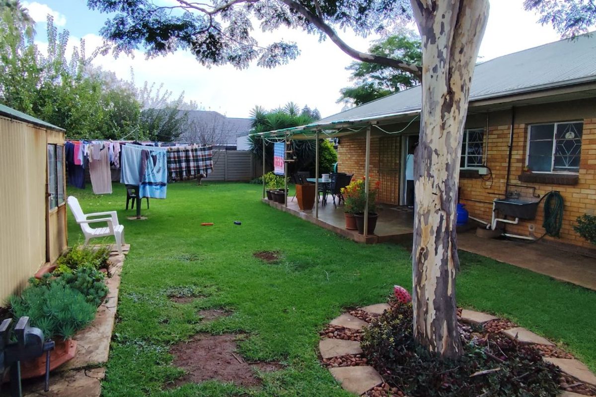 Rear garden view featuring a covered patio, brick exterior, established tree, and a small storage shed in a residential backyard setting.
