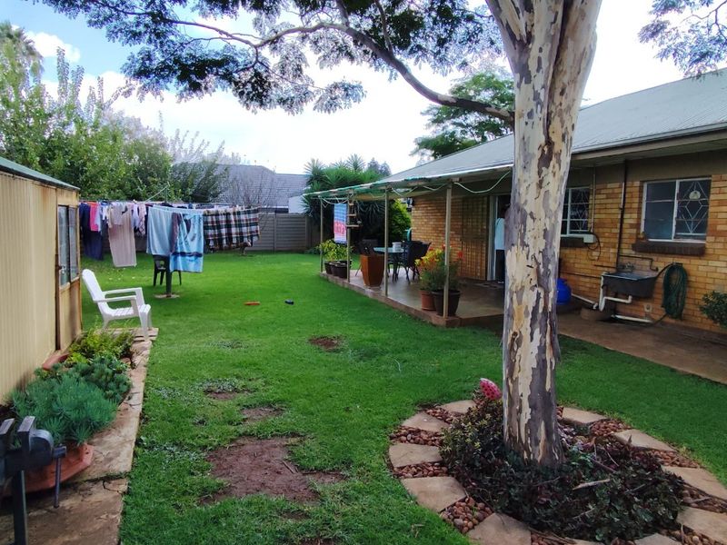 Rear garden view featuring a covered patio, brick exterior, established tree, and a small storage shed in a residential backyard setting.