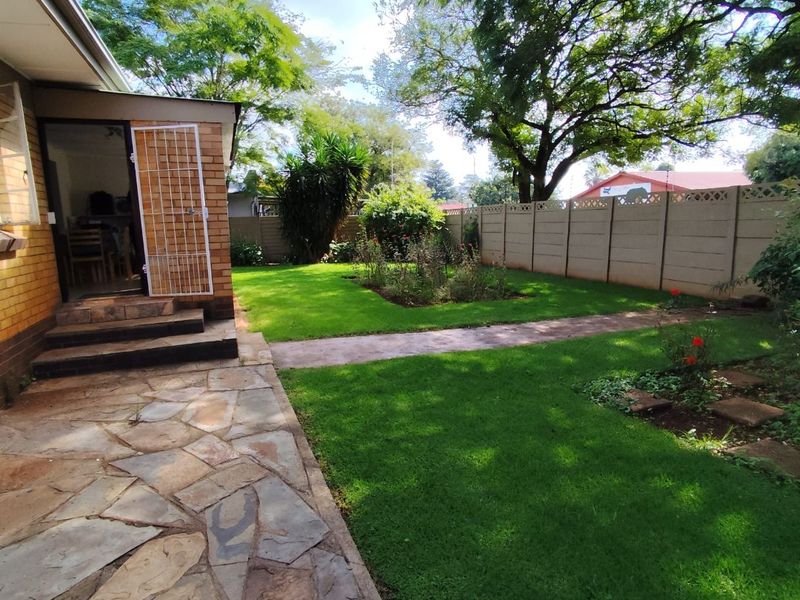 A well-maintained rear garden featuring a flagstone patio, lush lawn, established trees, and secure precast concrete boundary walling.