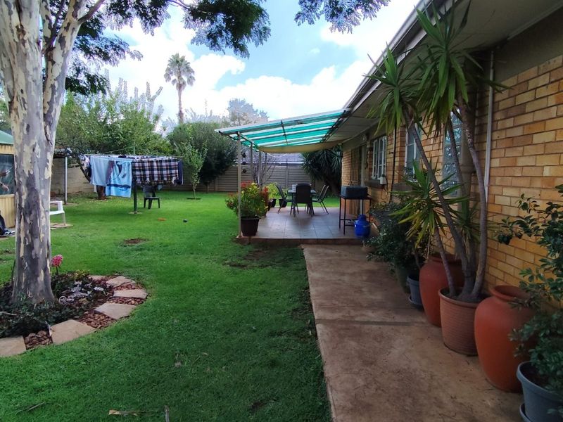 Rear view of the property featuring a brick facade, a covered patio area with a concrete walkway, and a spacious garden.