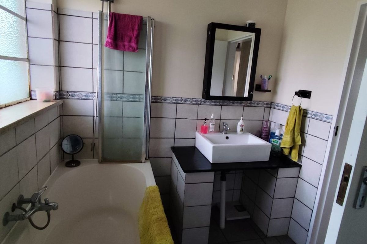 A functional bathroom featuring a bathtub with shower attachment, a vessel sink on a tiled vanity, and neutral wall tiling.