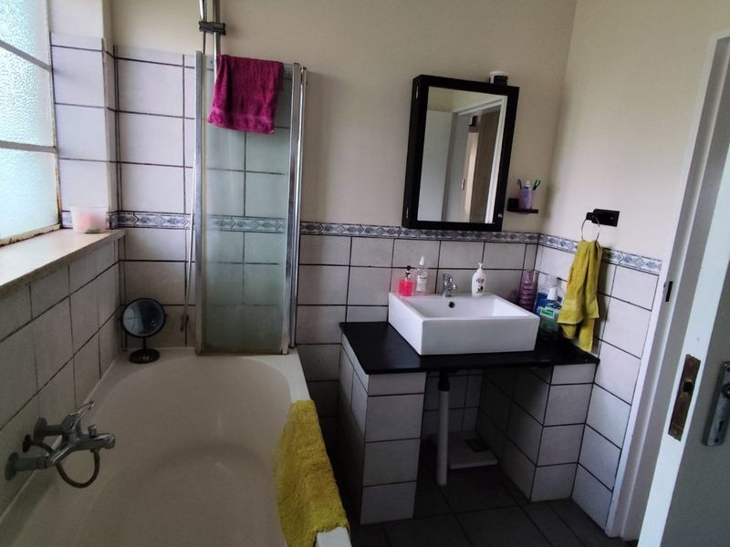 A functional bathroom featuring a bathtub with shower attachment, a vessel sink on a tiled vanity, and neutral wall tiling.