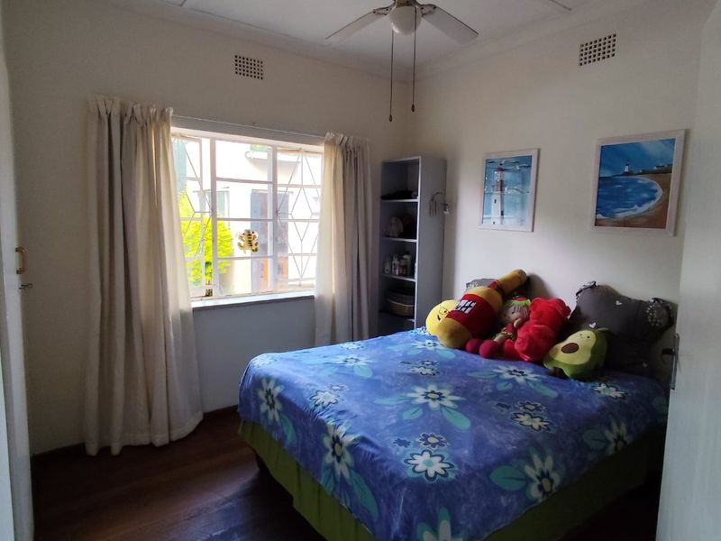 A bedroom featuring timber flooring, a ceiling fan, and security bars on the window, providing a functional and well-lit sleeping space.
