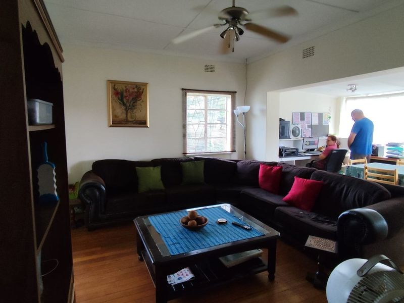 Open plan living area featuring hardwood flooring, a ceiling fan, and a secondary workspace area visible in the background.