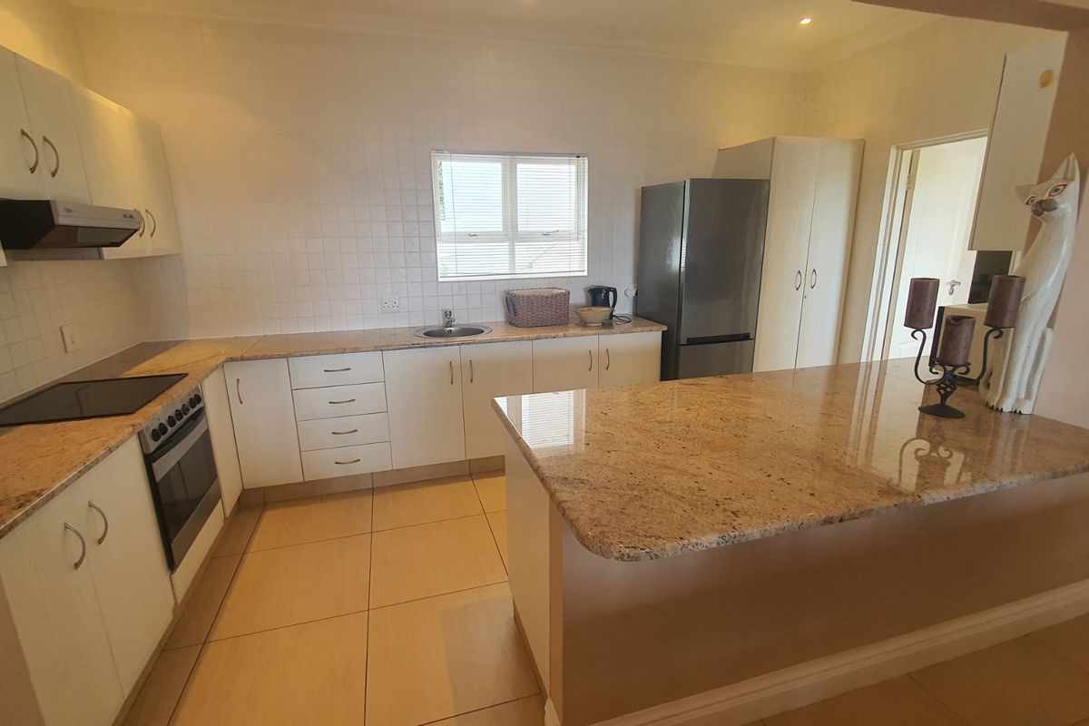 Functional kitchen featuring granite countertops, built-in oven, hob, extractor fan, and a breakfast bar, with tiled flooring and ample cabinetry.