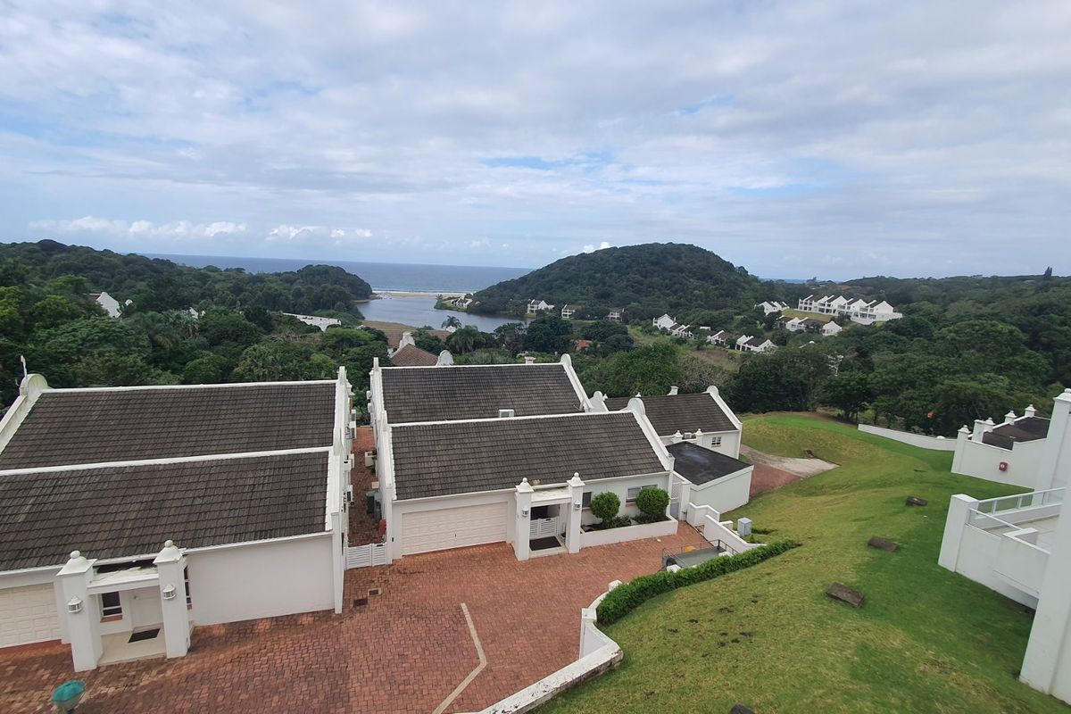 Aerial view of a townhouse complex featuring tiled roofs, brick paved driveways, and well-maintained green lawns with a scenic coastal landscape in the background.