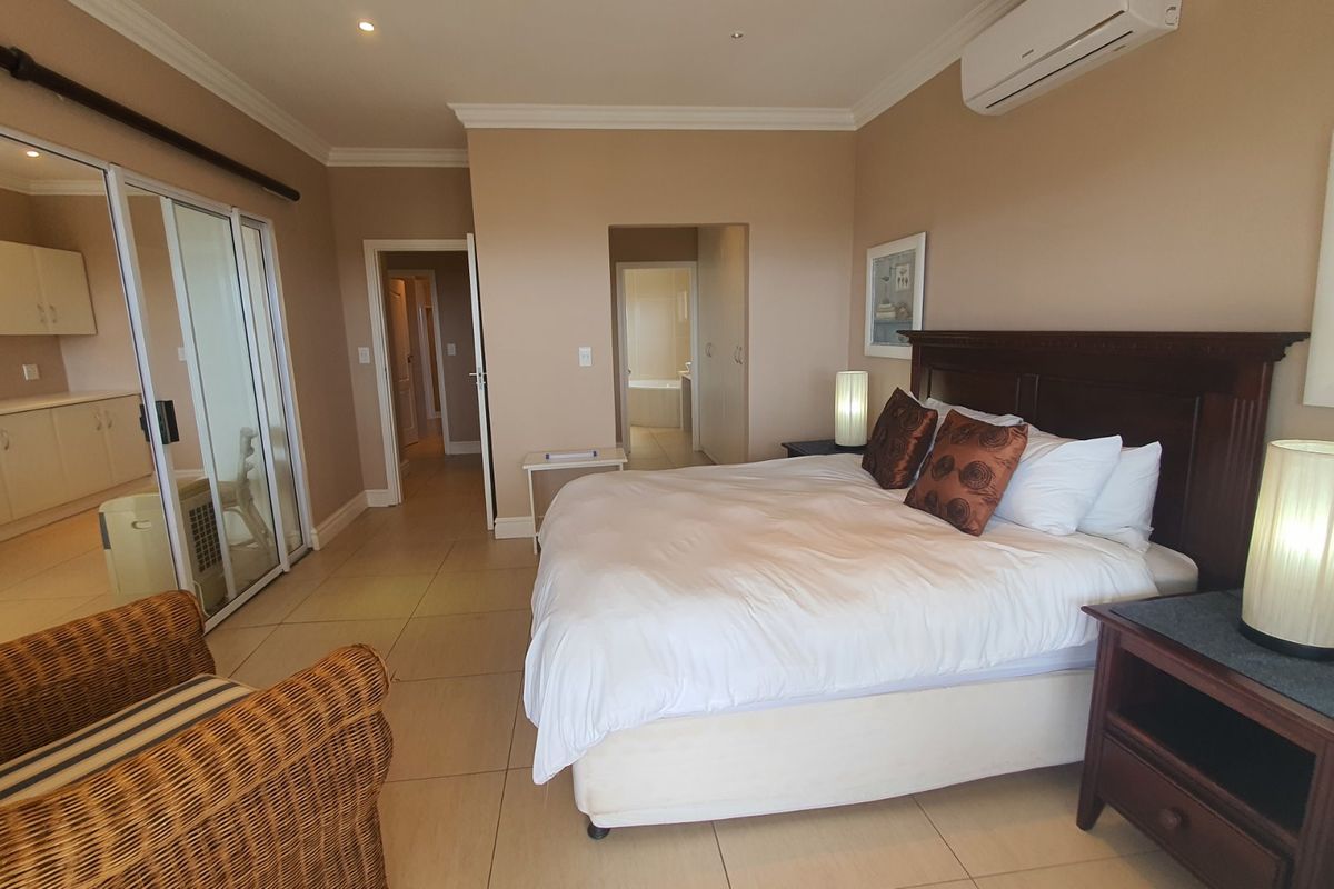 Spacious bedroom featuring tiled flooring, built-in cupboards, and a split-system air conditioner, with an adjoining ensuite bathroom and kitchenette area.