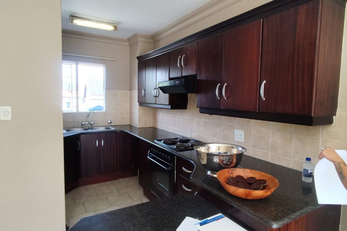A functional kitchen featuring dark wood cabinetry, granite countertops, built-in oven, hob, extractor fan, and tiled finishes.