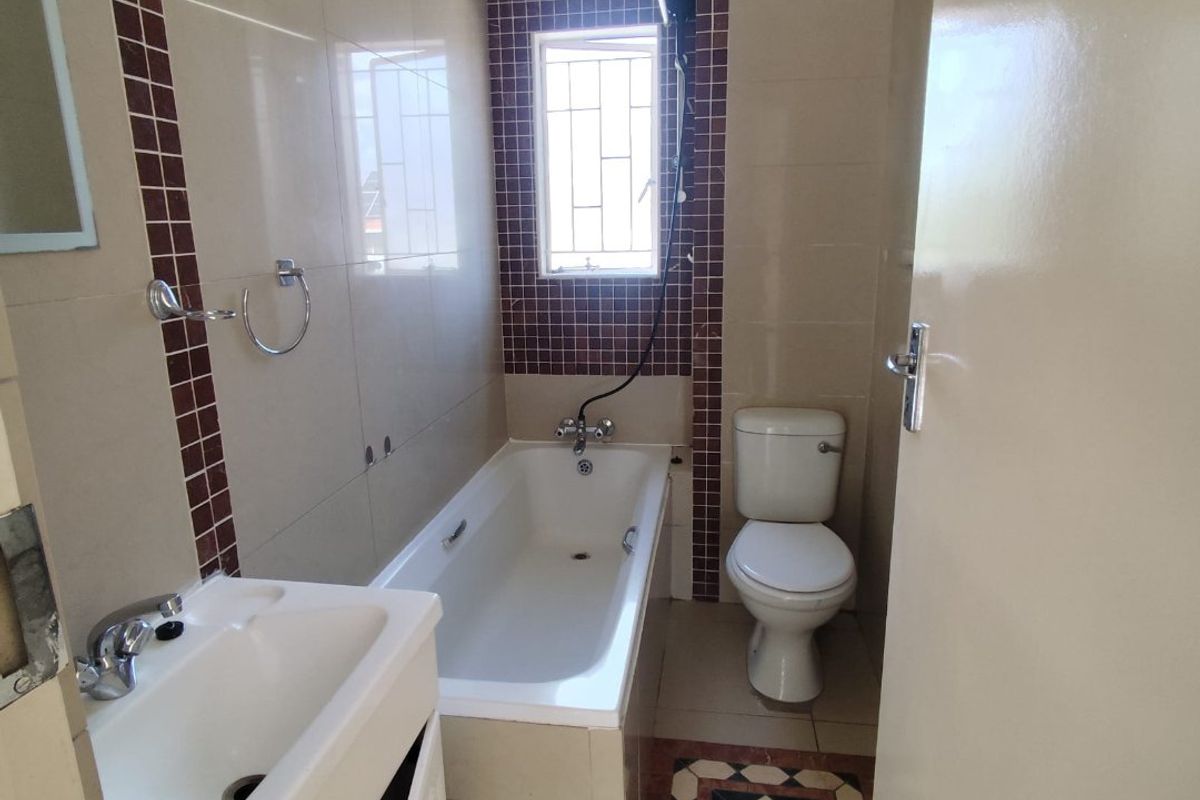 A functional bathroom featuring a bathtub, toilet, and vanity basin with tiled finishes and a window with security bars.