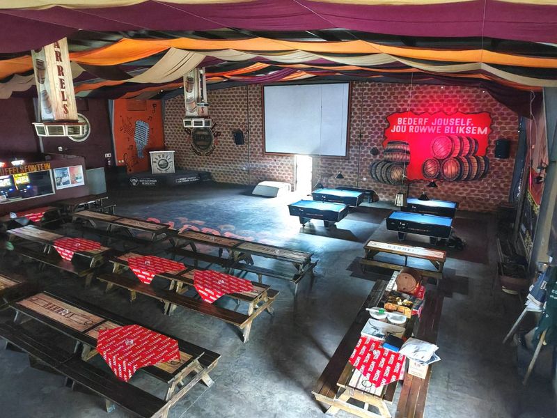 Spacious commercial clubhouse or event venue featuring exposed brick walls, a fabric-draped ceiling, concrete flooring, and a dedicated stage area with a projector screen.