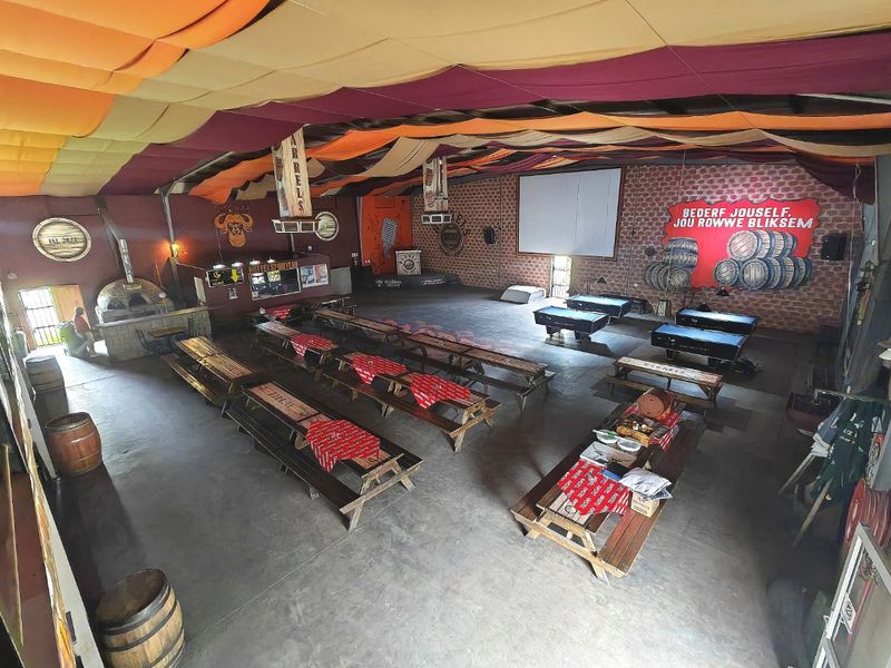 Spacious commercial clubhouse featuring a built-in pizza oven, bar area, exposed brick walls, and a decorative fabric ceiling canopy over concrete flooring.