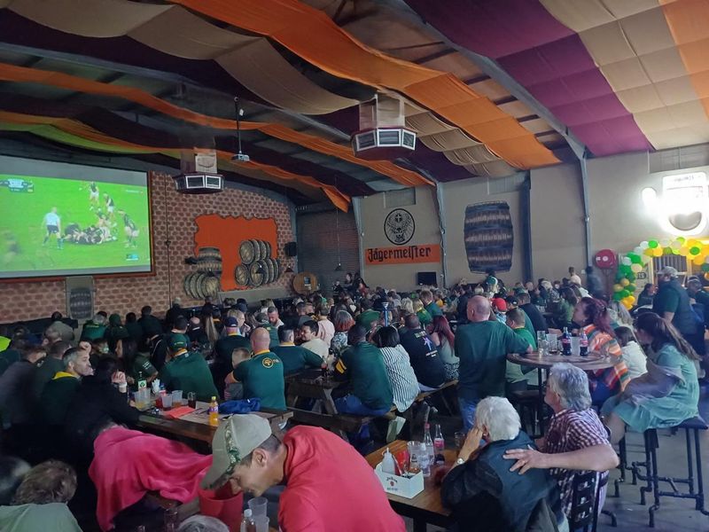 Spacious commercial clubhouse interior featuring high ceilings with fabric drapes, exposed steel trusses, and a large projector screen for entertainment.