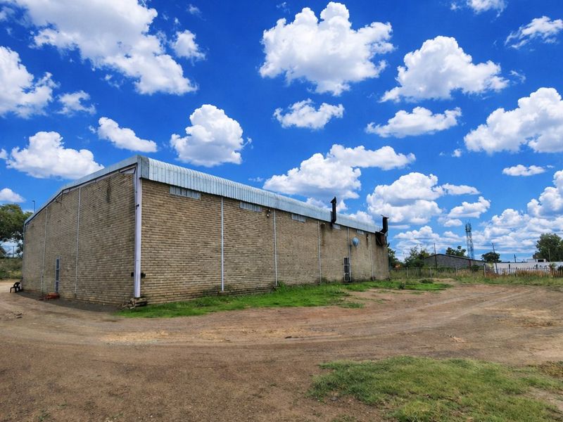 Rear view of a commercial warehouse building featuring brick construction and a metal roof, situated on an unpaved lot.