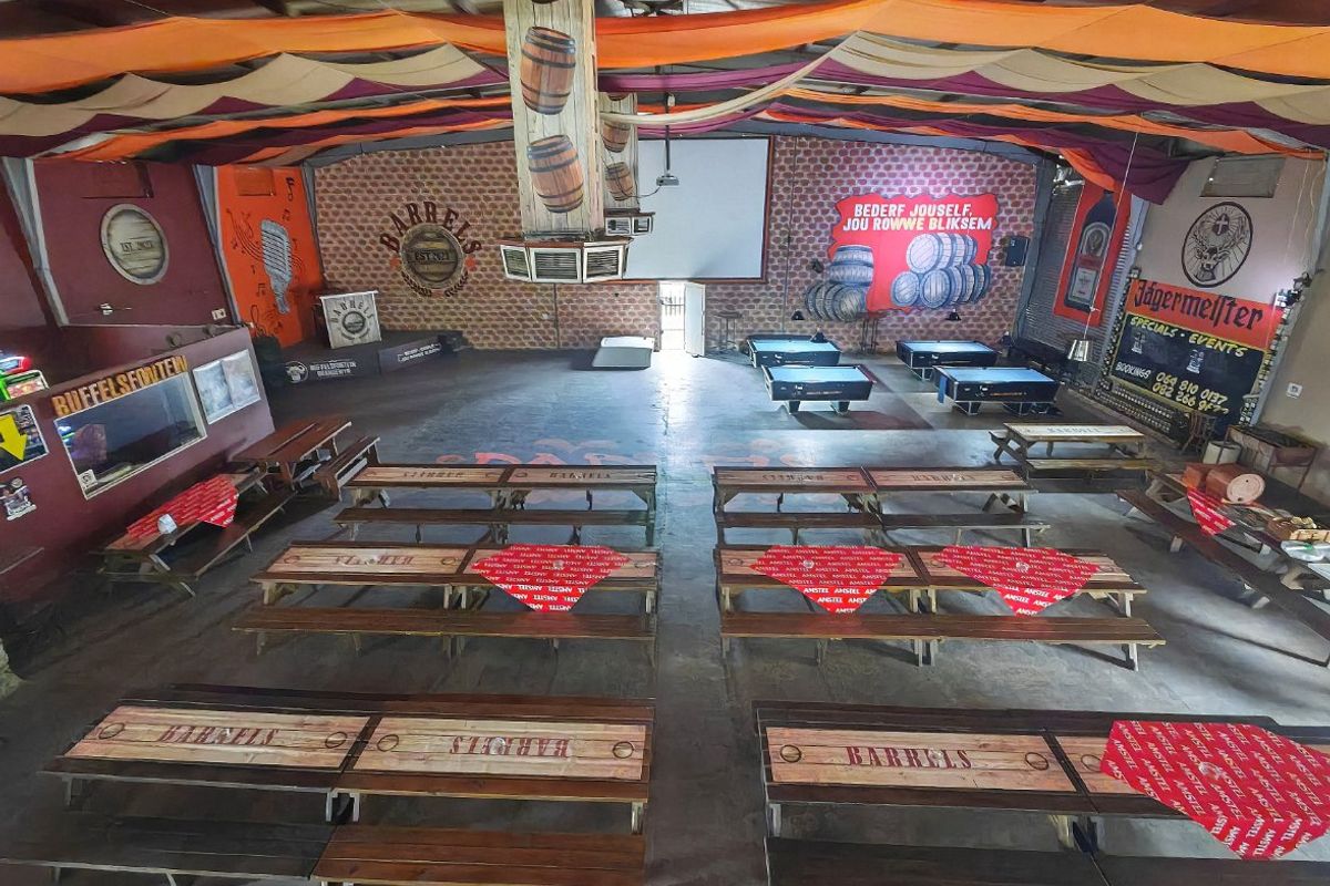 Spacious commercial clubhouse or event venue featuring high exposed ceilings, concrete floors, brick feature walls, and a built-in stage area.