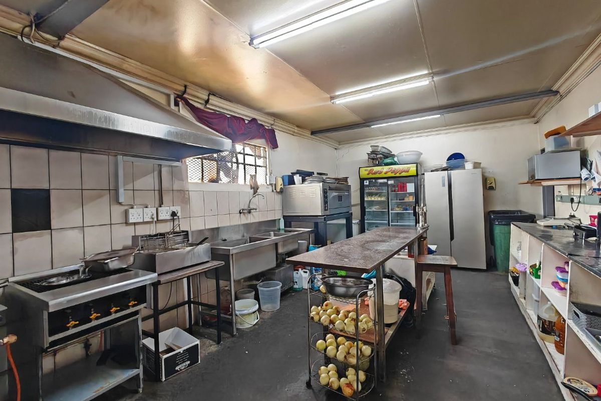Commercial kitchen space featuring stainless steel prep areas, double sink, gas cooking station, and integrated shelving, requiring maintenance and cosmetic updates.