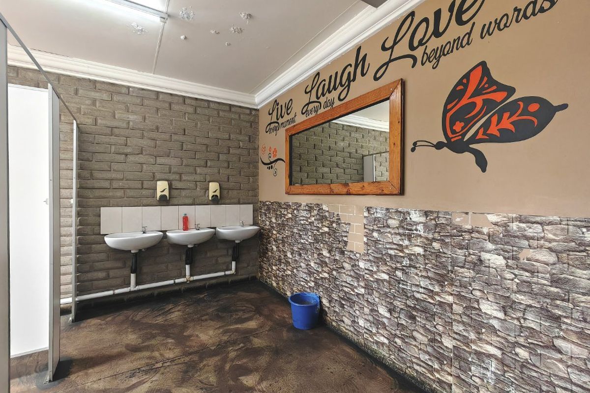Commercial bathroom facility featuring three wall-mounted basins, exposed brickwork, and decorative wall cladding, currently requiring maintenance and cosmetic updates.