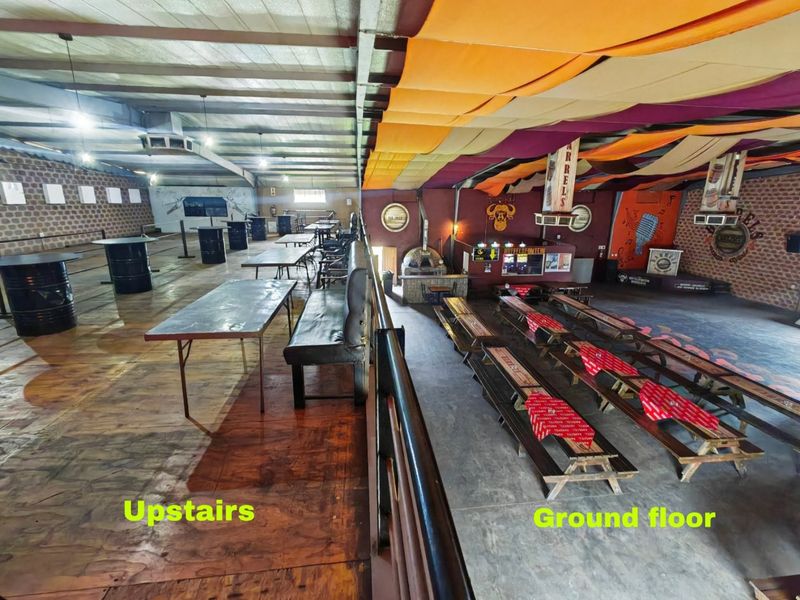 A split-level commercial open-plan space featuring a mezzanine level with timber flooring overlooking a ground floor area with concrete floors and a pizza oven.