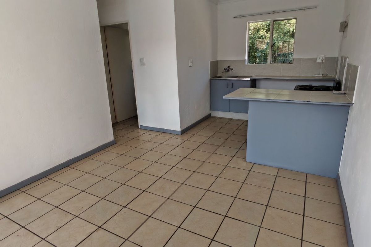 An empty open-plan kitchen and living area featuring tiled flooring, a breakfast bar, and basic cabinetry, offering a blank canvas for renovation.