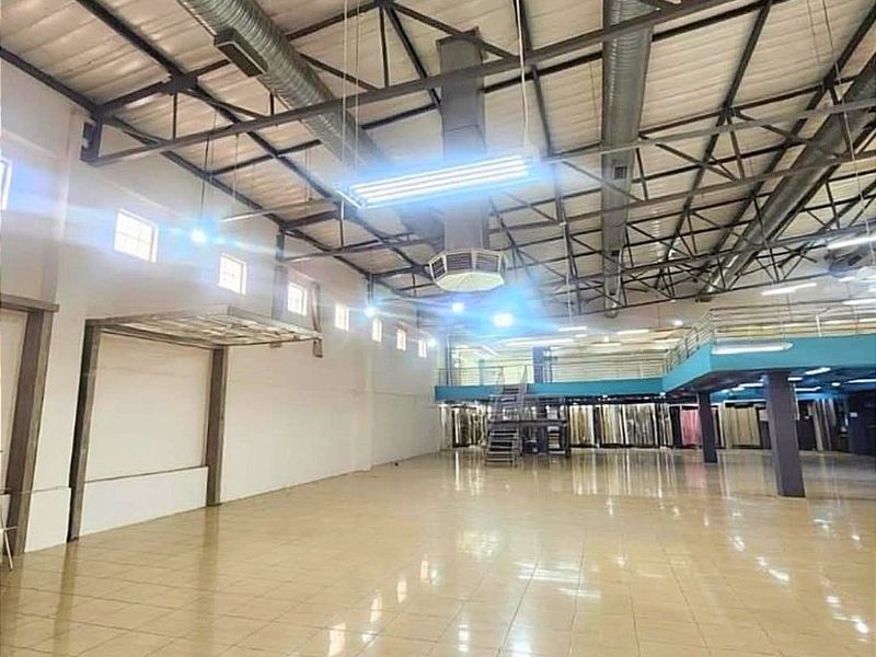 Spacious commercial warehouse or showroom featuring high ceilings with exposed steel trusses, tiled flooring, a mezzanine level, and integrated HVAC ducting.